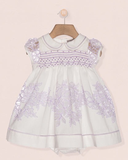 White baby dress with purple floral embroidery on a beige background