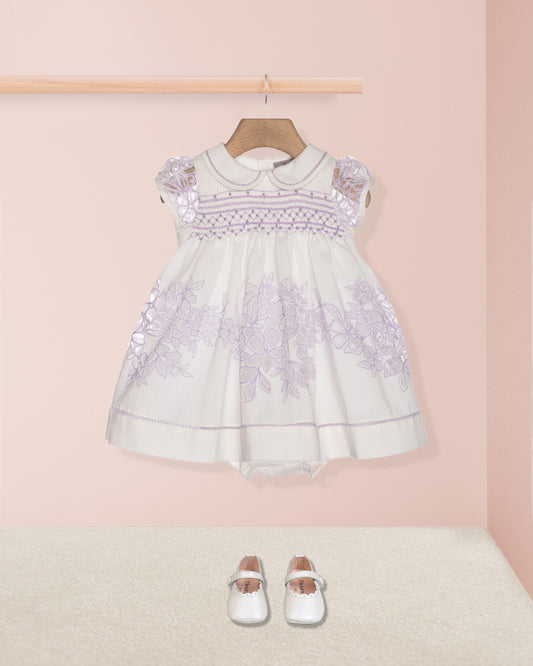 White lace dress with purple floral embroidery on a pink background