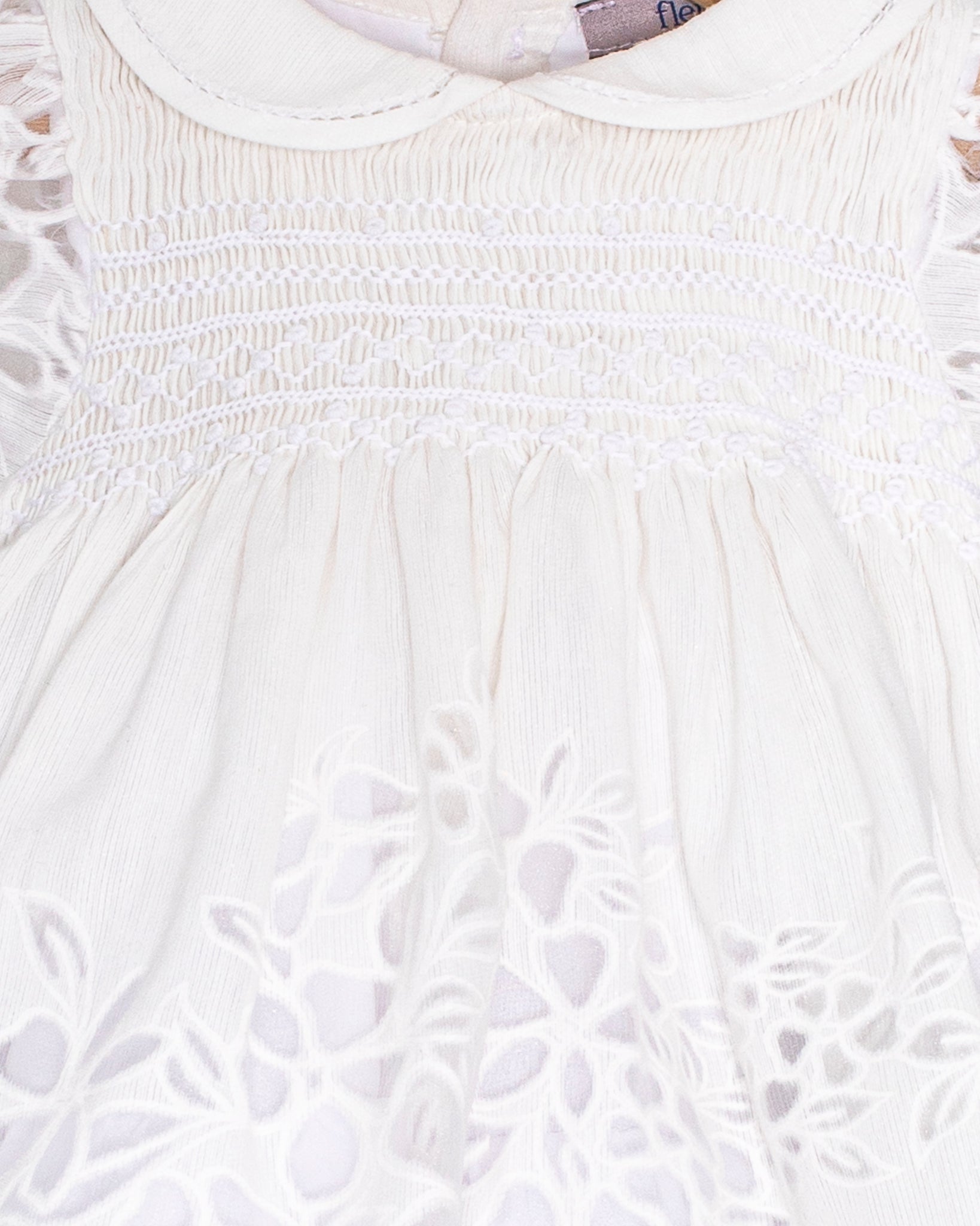 Close-up of the Baby Emmy Doppia White Smock Dress bodice, highlighting the hand-smocked panel and floral laser-cut embroidery.