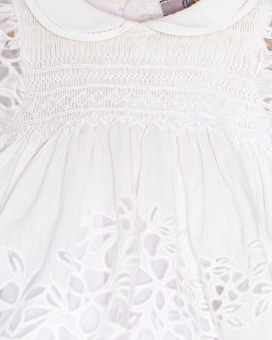 Close-up of the Baby Emmy Doppia White Smock Dress bodice, highlighting the hand-smocked panel and floral laser-cut embroidery.