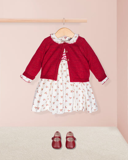 Red sweater over a white dress with floral pattern, paired with red shoes on a pink background