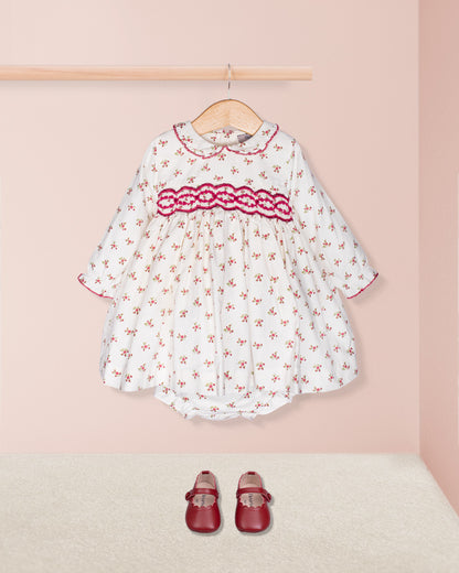 White dress with red floral pattern and matching shoes on a pink background
