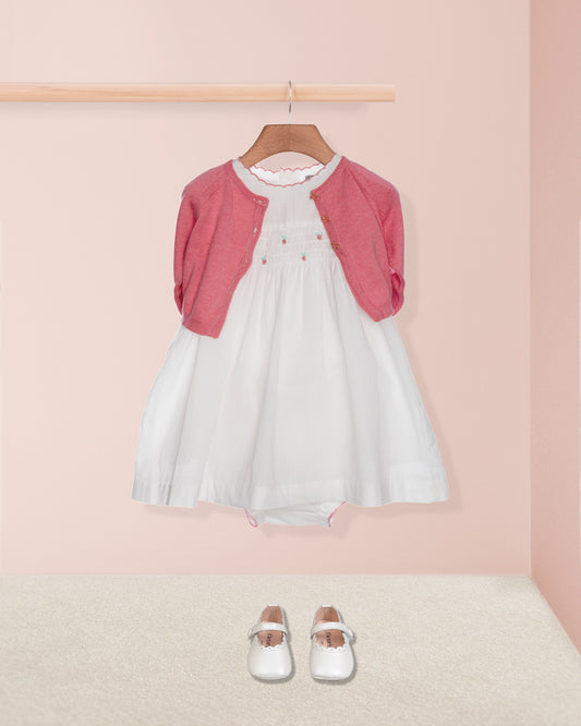 White dress with pink cardigan and white shoes on a pink background
