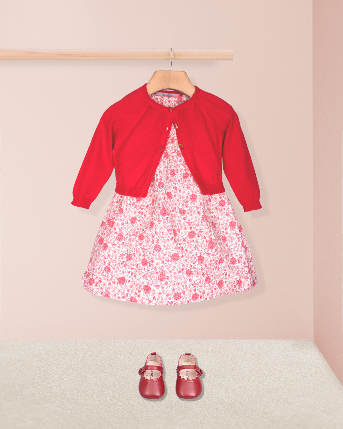 Red cardigan over a floral dress with matching shoes on a pink background