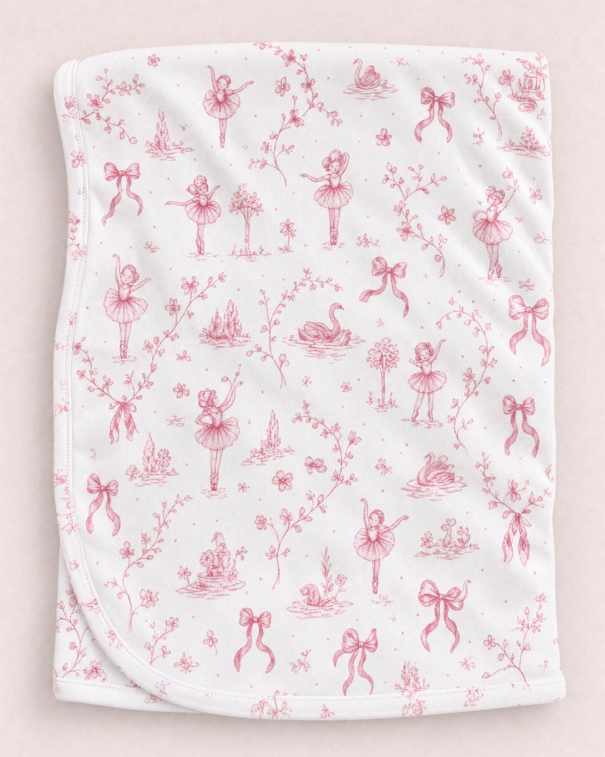 White blanket with pinkish red ballerinas, swans and bows, agaist a peach neutral background.
