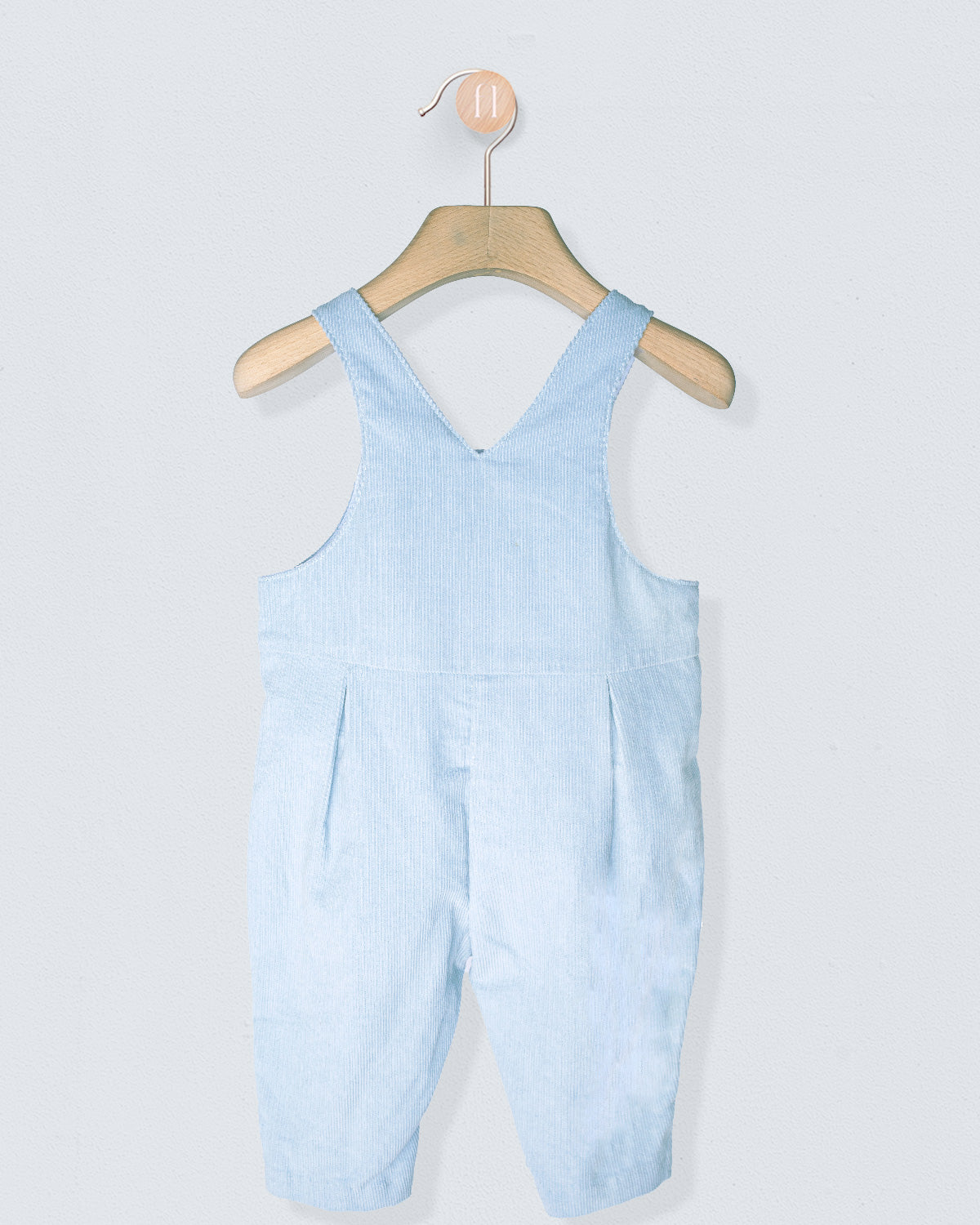 Light blue overalls hanging on a wooden hanger against a light gray background