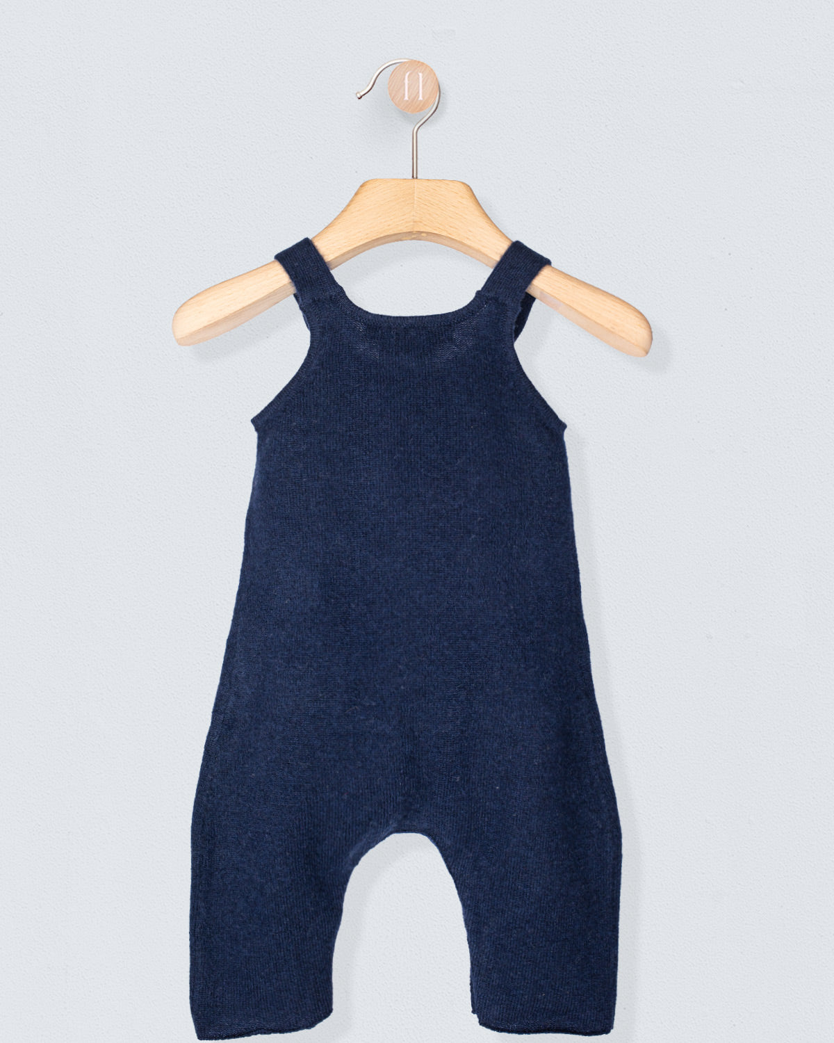 Navy blue baby romper on a wooden hanger against a light gray background