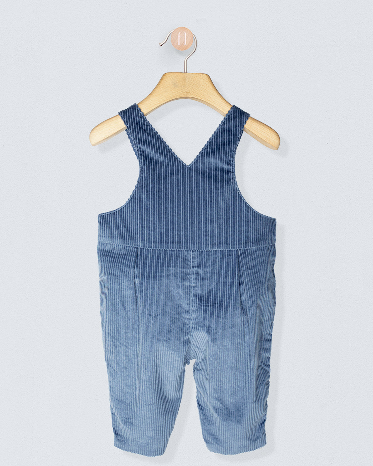 back of blue corduroy overalls on a wooden hanger against a light gray background