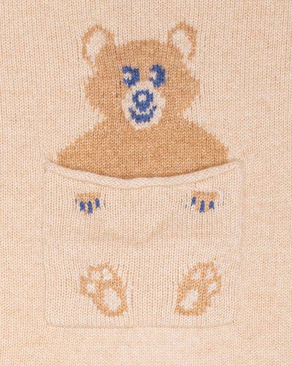Close up of embroidered design of a bear peeking out from a pocket on a beige cashmere blanket