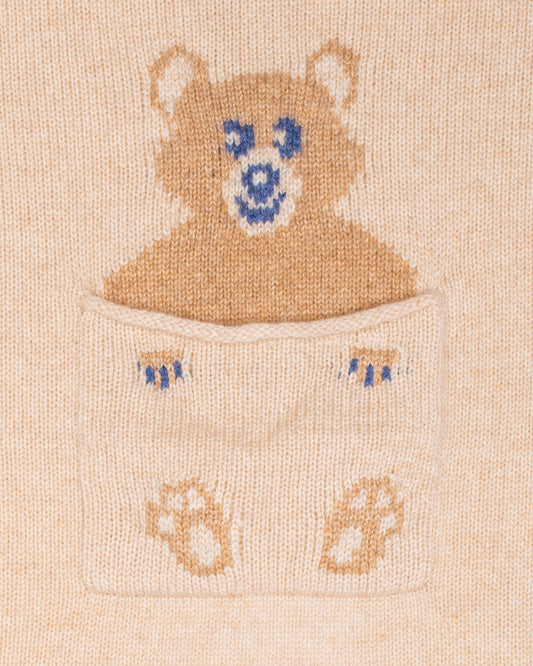 Close up of embroidered design of a bear peeking out from a pocket on a beige cashmere blanket