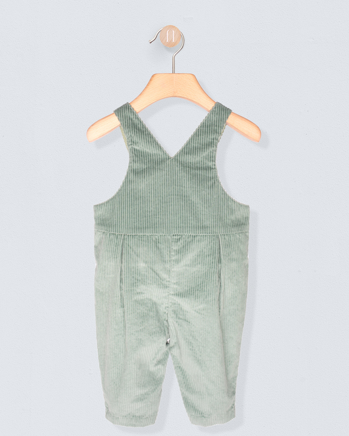 Back of Green corduroy overalls on a wooden hanger against a light gray background