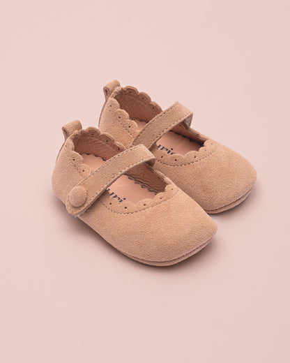 Pair of beige baby shoes with a strap on a pink background