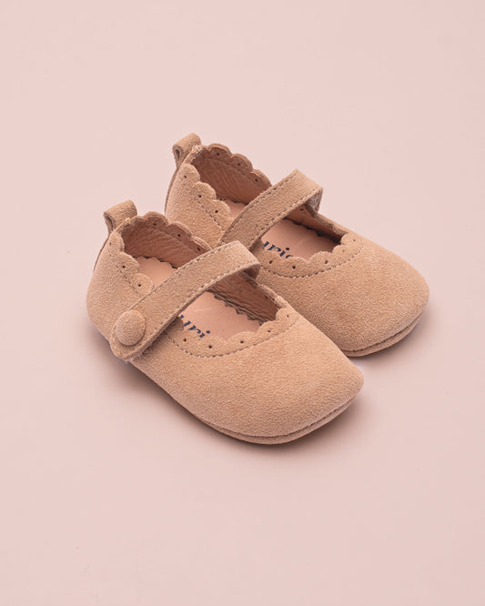 Pair of beige baby shoes with a strap on a pink background