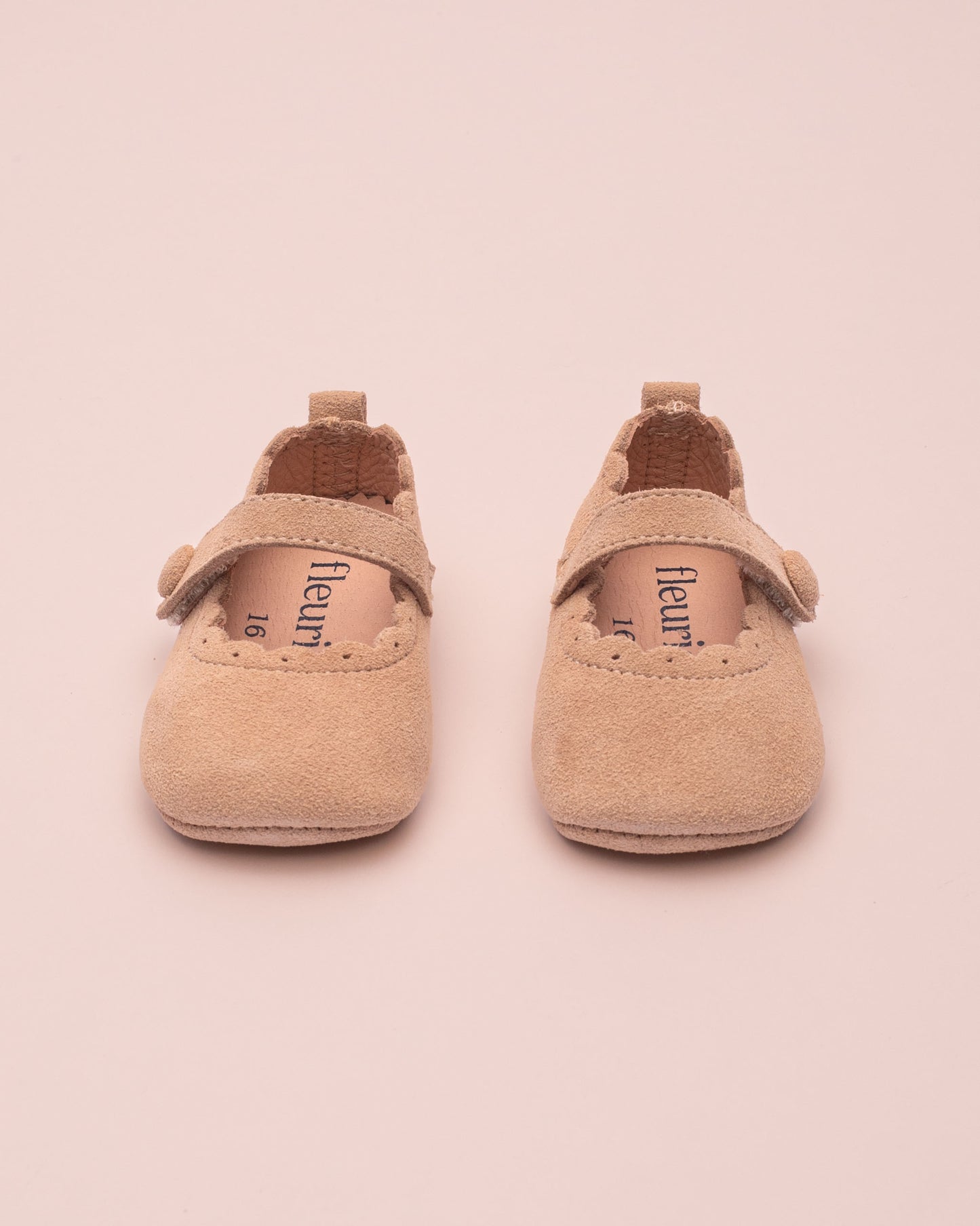 Pair of beige baby shoes with 'fleuret' branding on a pink background