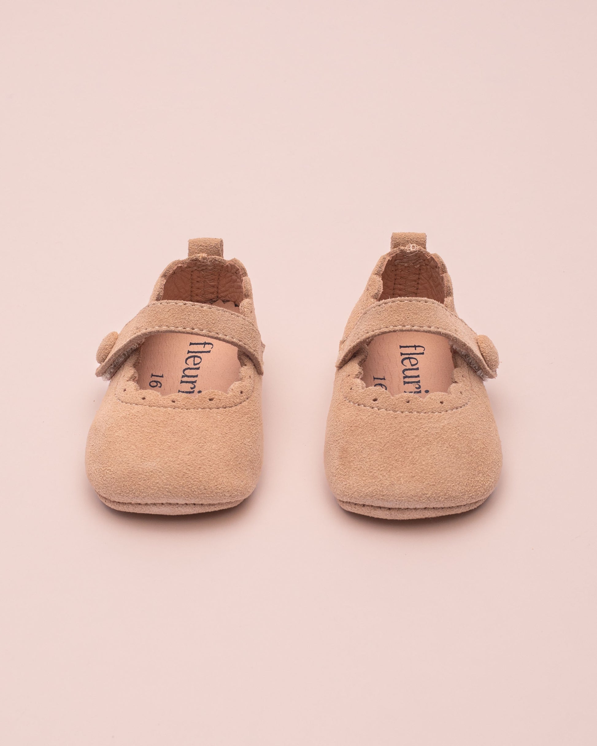 Pair of beige baby shoes with 'fleuret' branding on a pink background