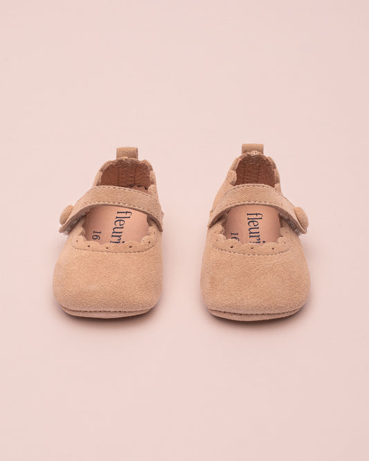 Pair of beige baby shoes with 'fleuret' branding on a pink background
