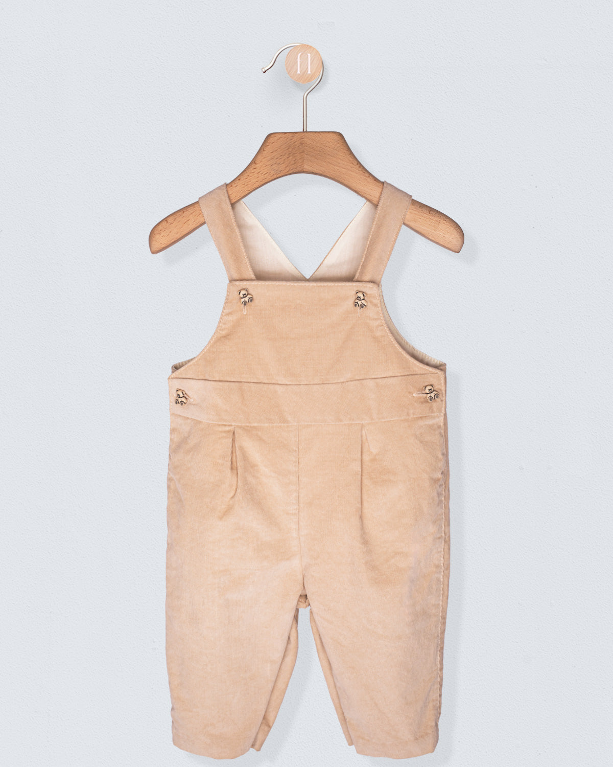 Beige overalls hanging on a wooden hanger against a light gray background