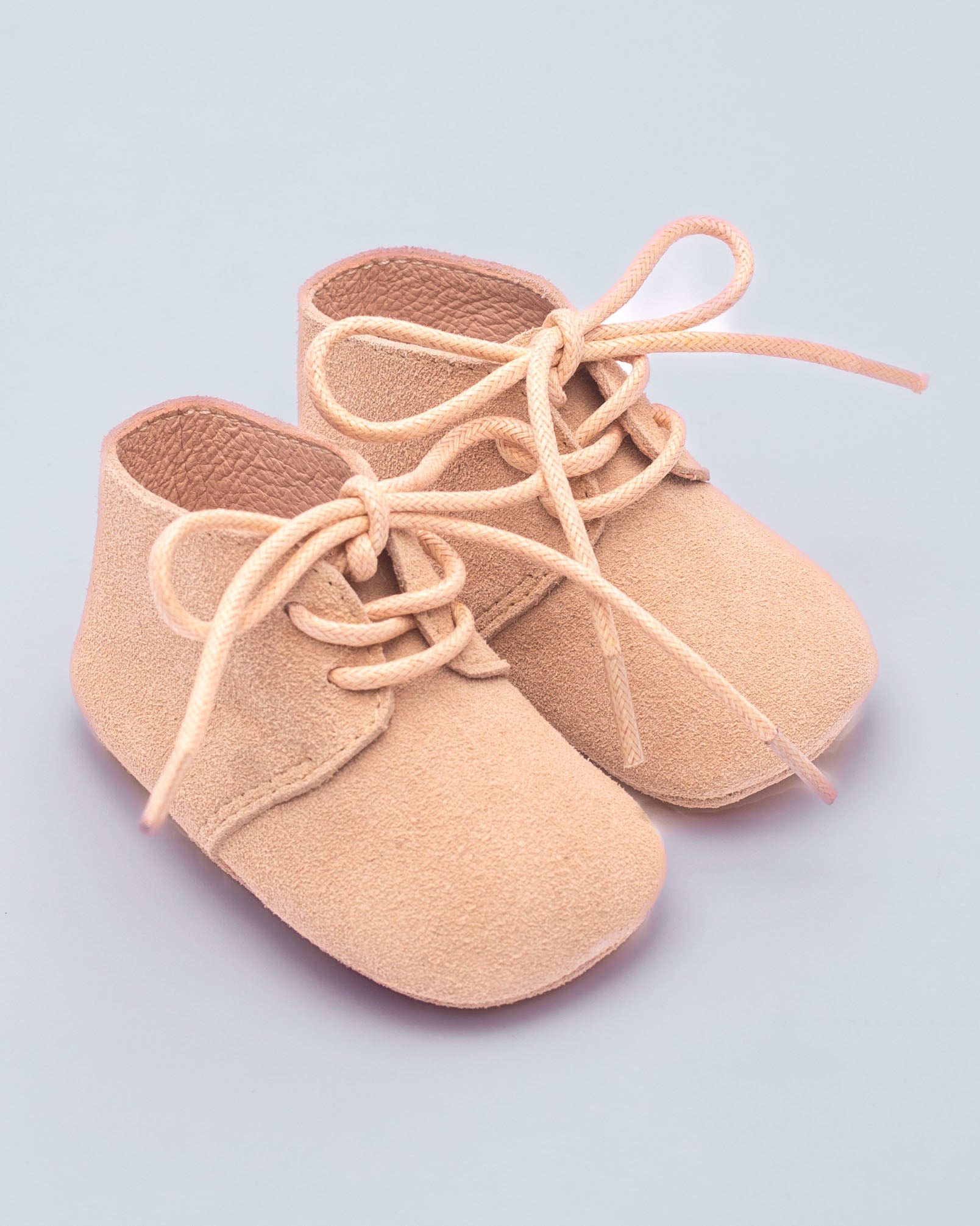 Pair of beige baby shoes with laces on a light purple background