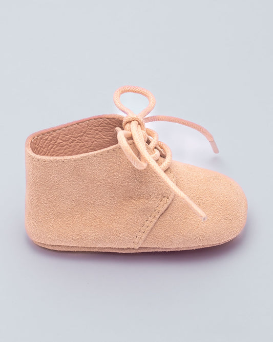 Beige baby shoe with a lace on a light purple background side view