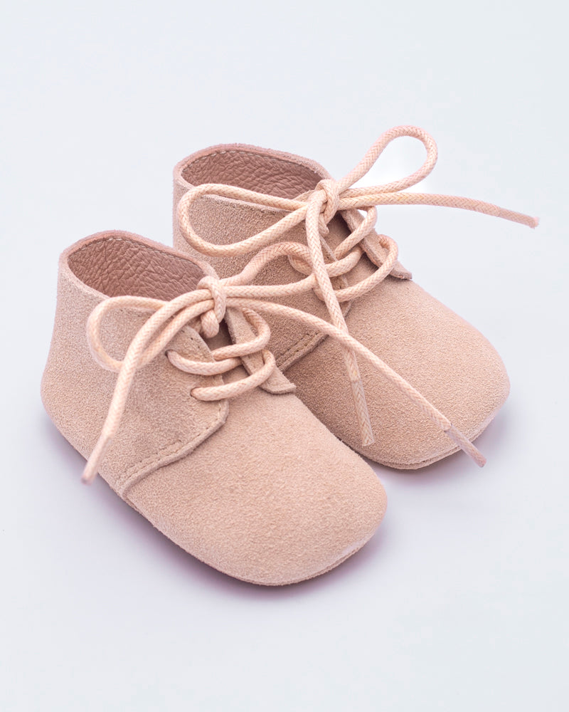 Beige baby shoes with laces on a light gray background