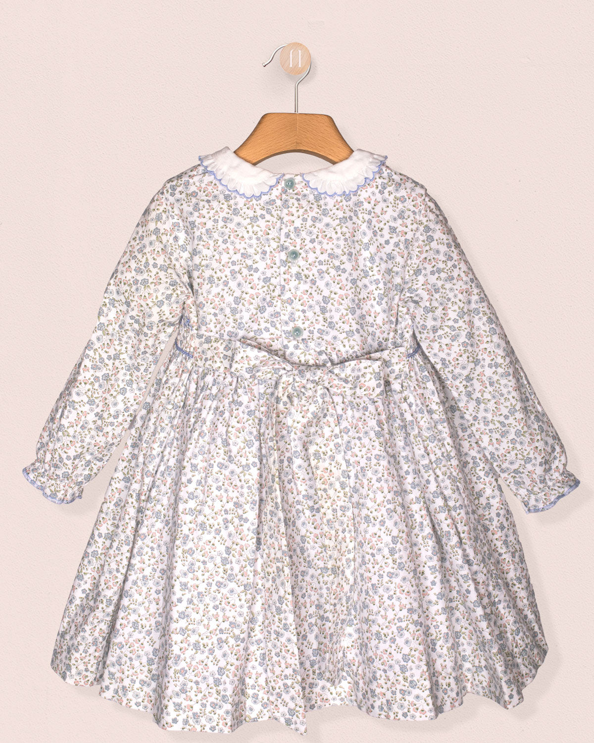 A back view of the Fiorella Belina dress showing the matching fabric bow at the waist and invisible zipper closure. The same dainty blue floral print covers the full dress.