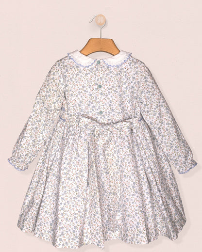 A back view of the Fiorella Belina dress showing the matching fabric bow at the waist and invisible zipper closure. The same dainty blue floral print covers the full dress.