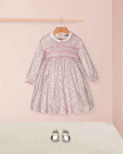 Full front view of the smocked floral dress paired with silver shoes, shown hanging without the cardigan for a simple and timeless look.