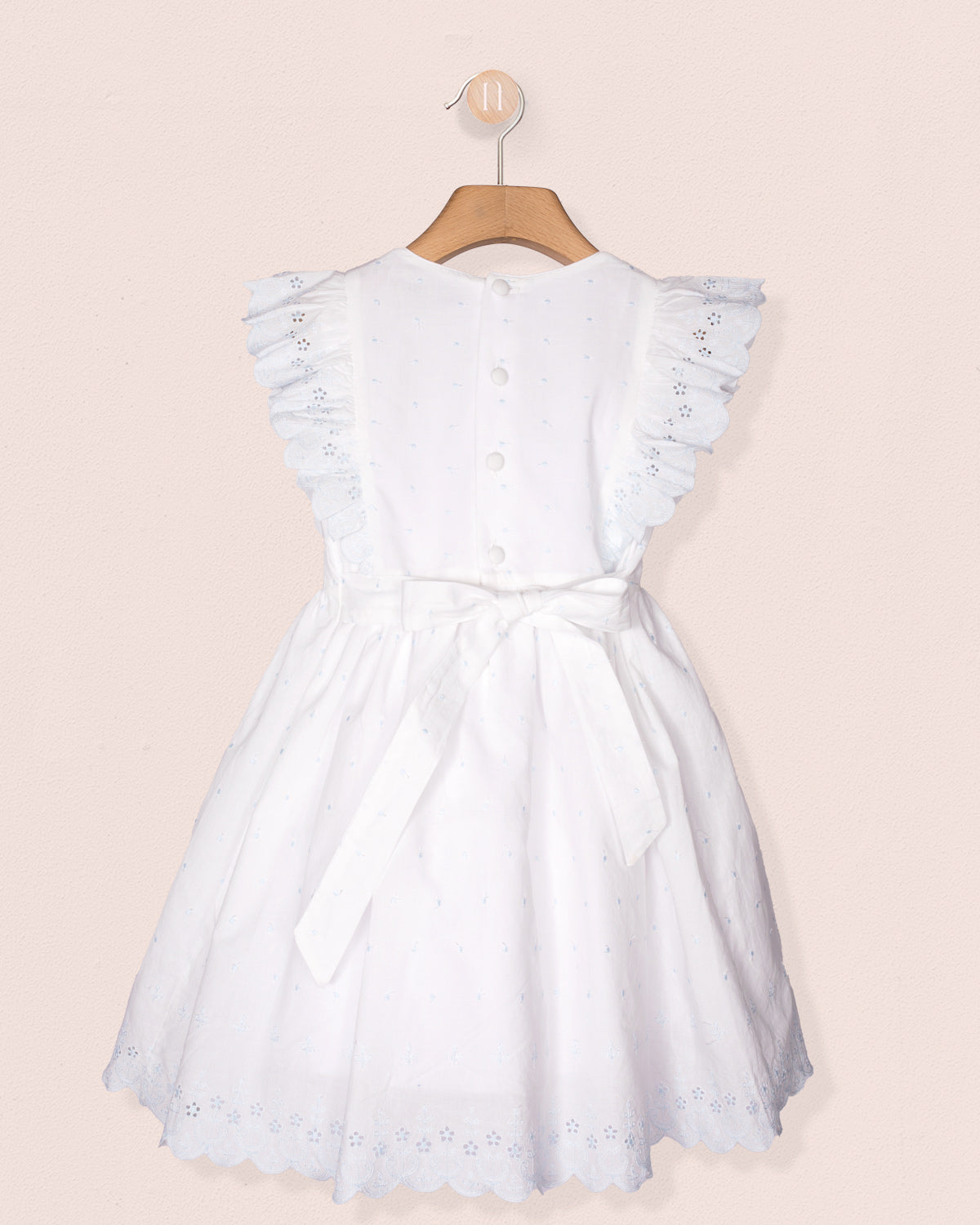White dress with lace details on a hanger against a light pink background