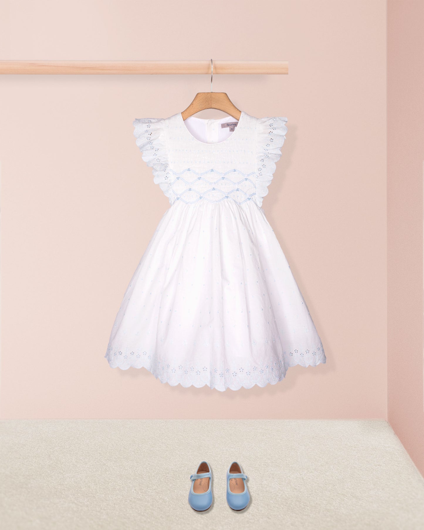 White dress with ruffled sleeves on a hanger against a pink wall with blue shoes on the floor.