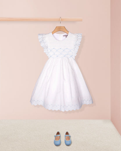 White dress with ruffled sleeves on a hanger against a pink wall with blue shoes on the floor.