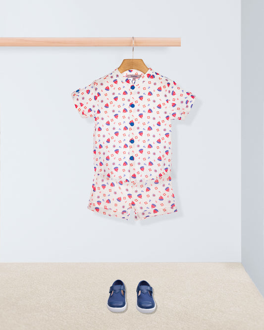 Short sleeve white shirt with red and blue boats with matching shorts, on a hanger with blue shoes on the floor below