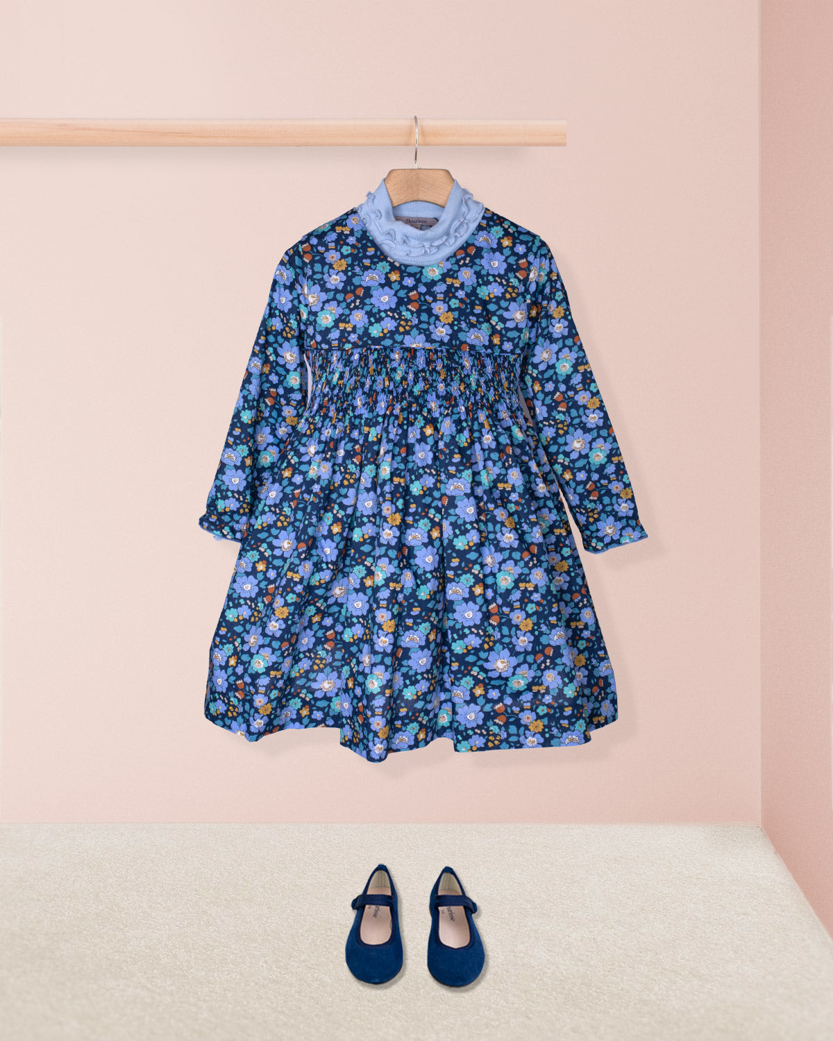 Blue floral dress on a hanger with matching shoes on the floor against a pink wall.
