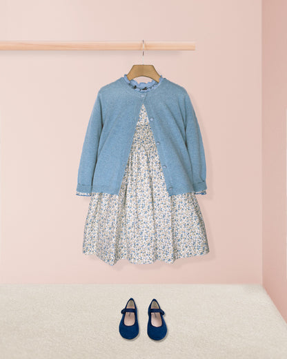 Blue cardigan over a floral dress with matching shoes on a pink background