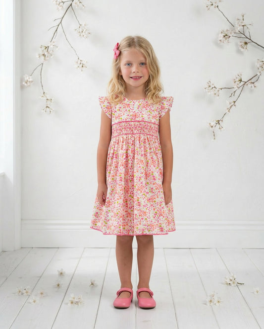 Young girl wearing a floral dress standing on a white floor with decorative branches.