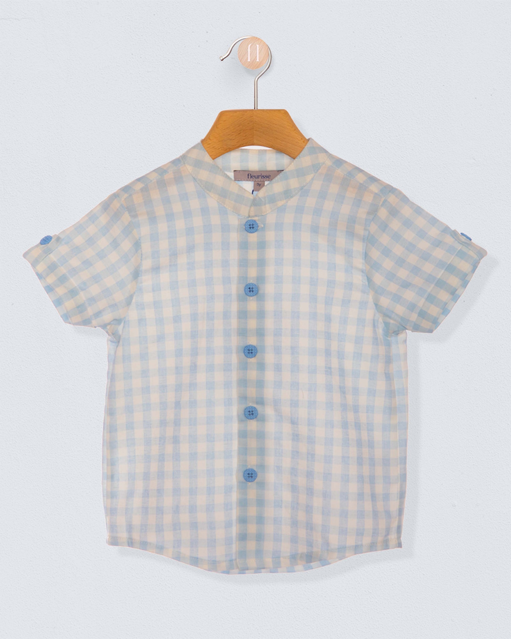 light blue and white checkered shirt with blue buttons on a wooden hanger against a light blueish grey backdrop
