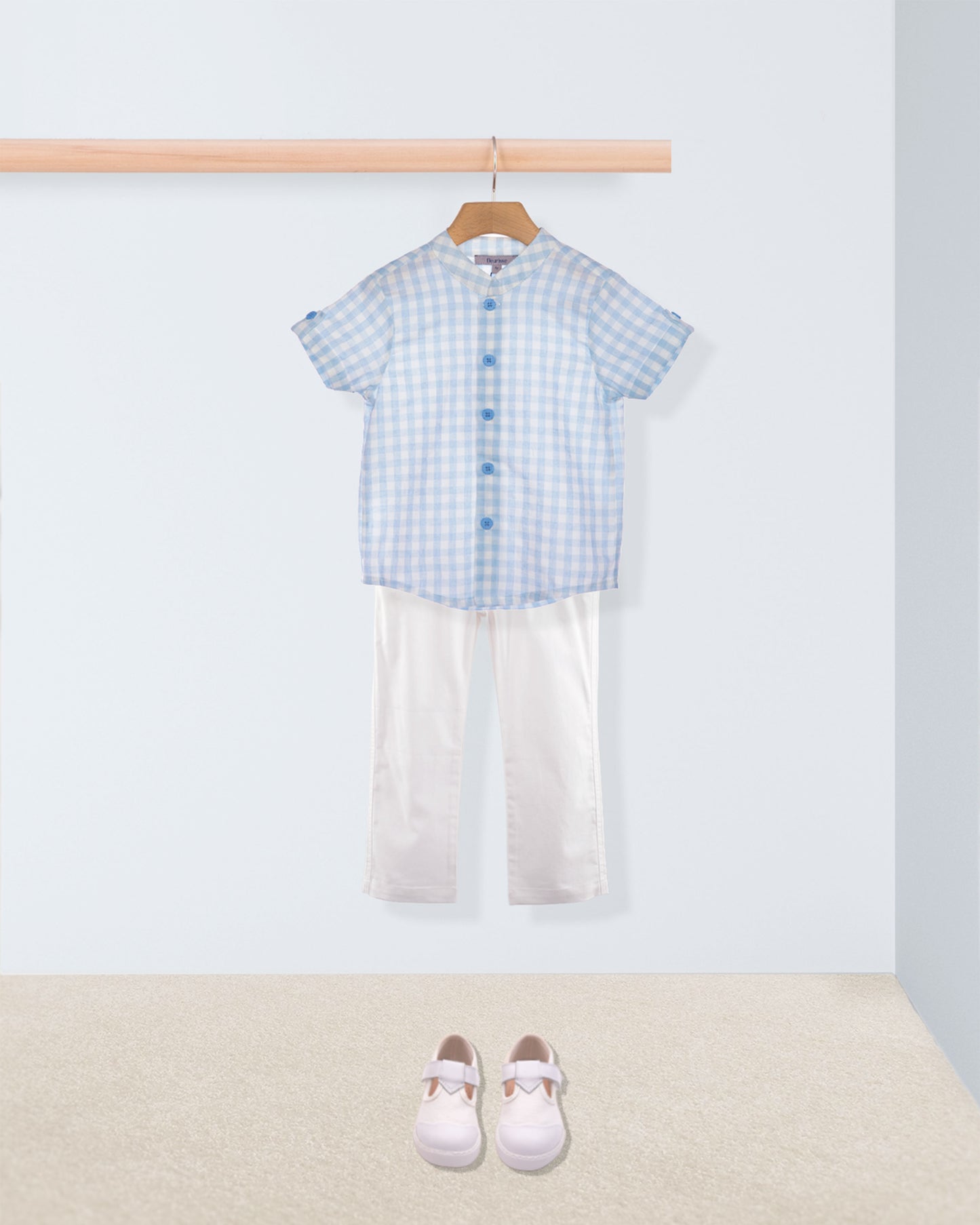 Children's outfit with blue checkered shirt and white pants on a hanger, with shoes on the floor.