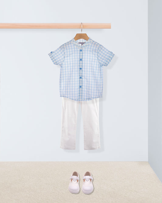 Children's outfit with blue checkered shirt and white pants on a hanger, with shoes on the floor.