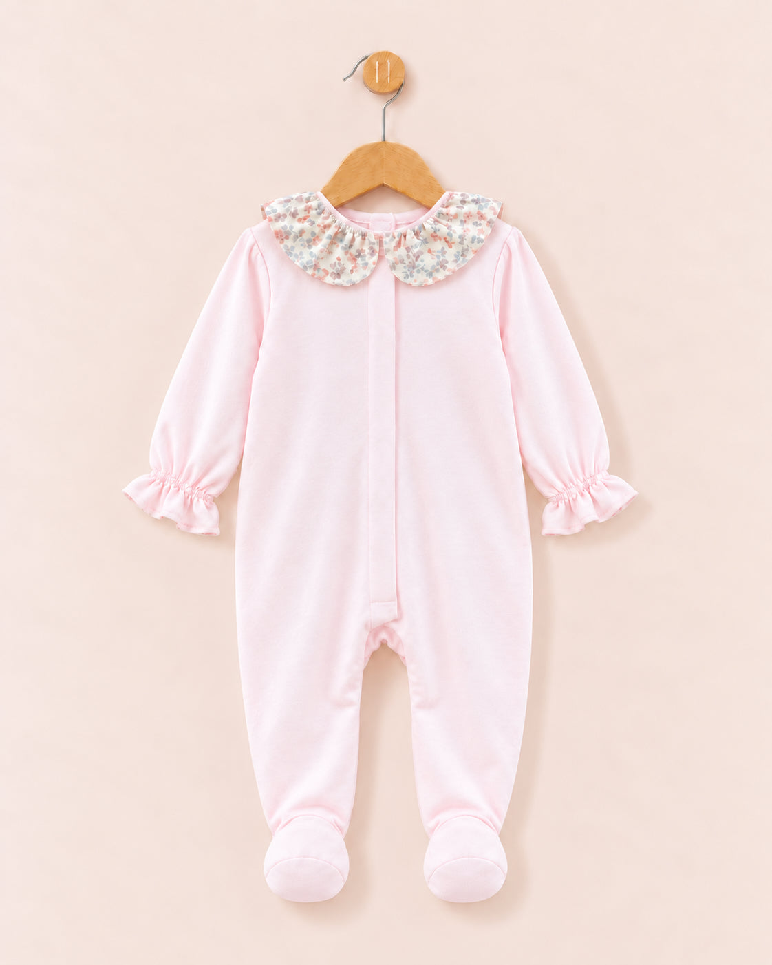 A baby footed sleeper in light pink fleece, featuring a floral-patterned Peter Pan collar and ruffled cuffs, hanging on a wooden hanger against a solid pale pink background.