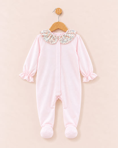 A baby footed sleeper in light pink fleece, featuring a floral-patterned Peter Pan collar and ruffled cuffs, hanging on a wooden hanger against a solid pale pink background.