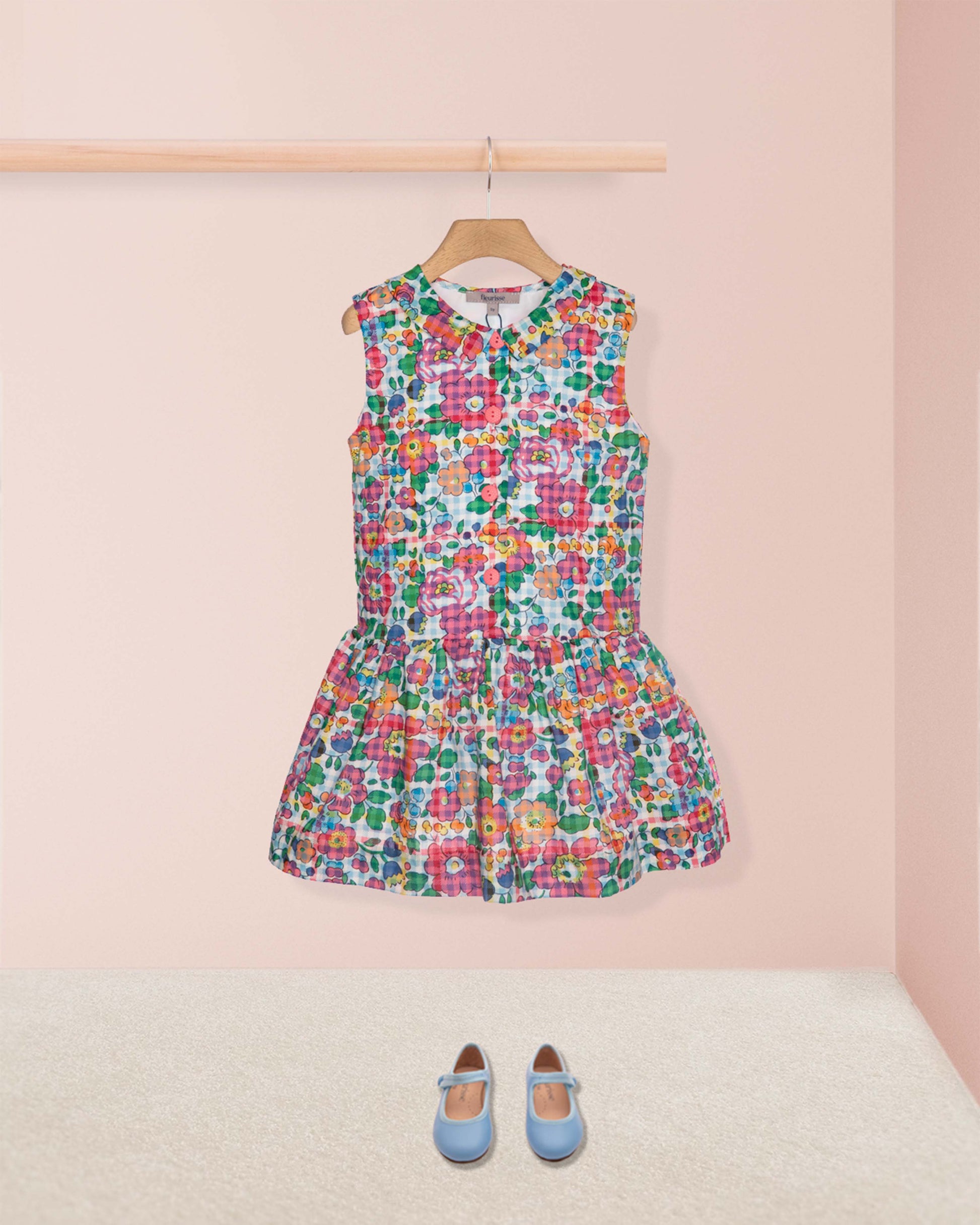 Colorful floral dress on a hanger against a pink wall with blue shoes on the floor.