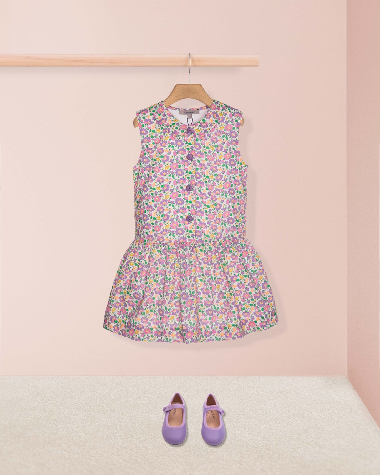 Floral dress on a hanger with purple shoes on a pink background