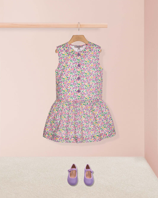 Floral dress on a hanger with purple shoes on a pink background