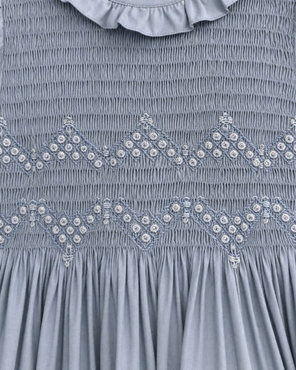 Close-up of a blue smocked dress featuring decorative embroidered diamond patterns with small white bead accents and a ruffled collar.