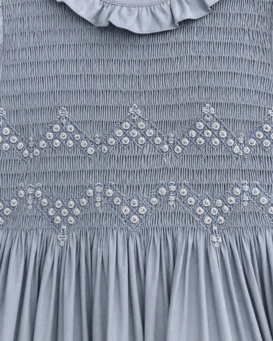 Close-up of a blue smocked dress featuring decorative embroidered diamond patterns with small white bead accents and a ruffled collar.
