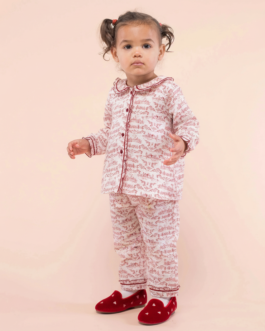 Child wearing a red and white patterned outfit with red shoes on a pink background