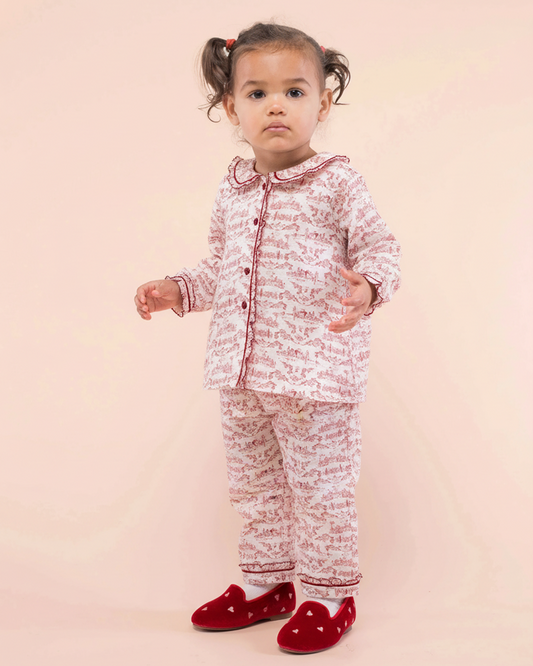 Child wearing a red and white patterned outfit with red shoes on a pink background
