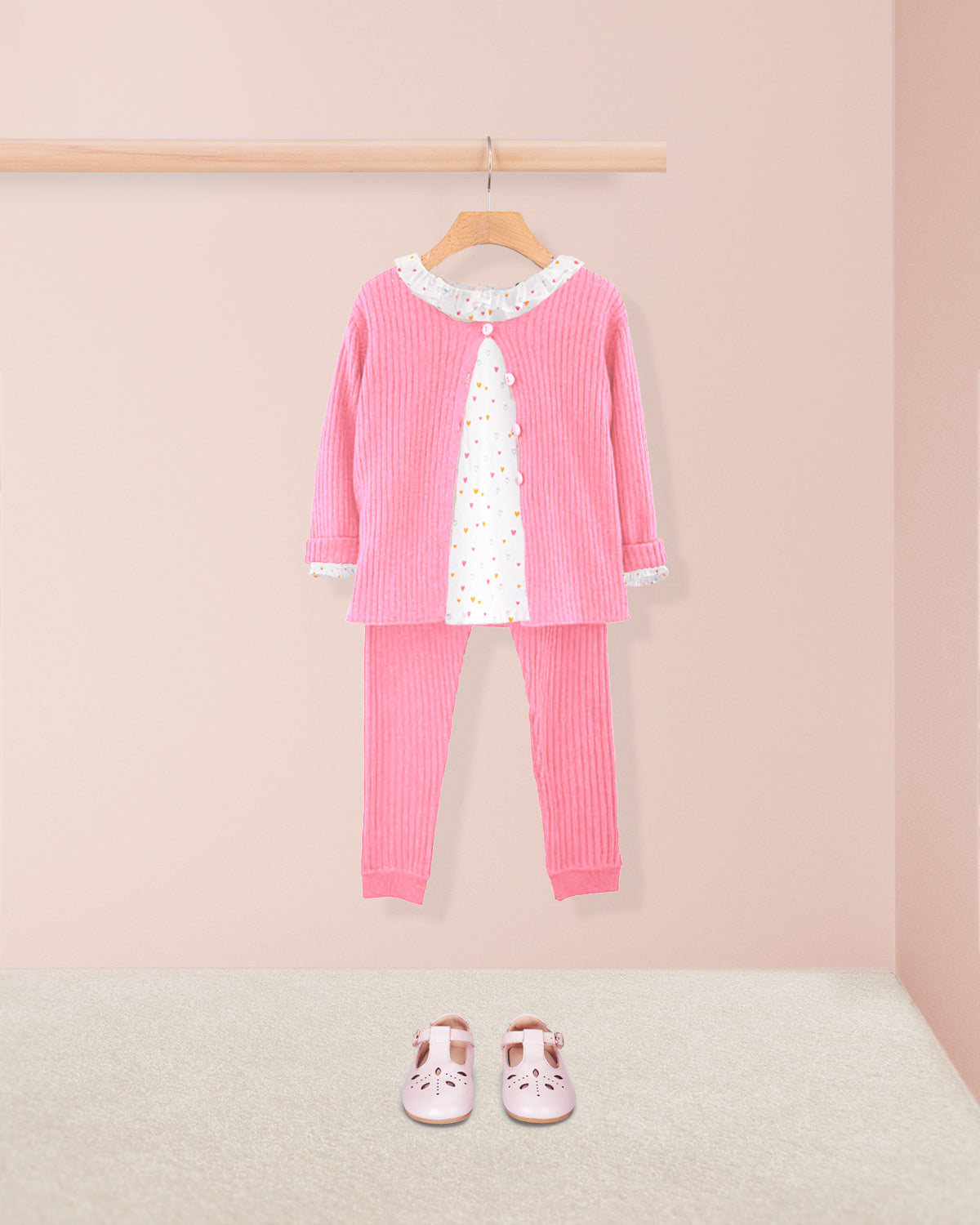 Pink children's outfit with a matching cardigan, top, and pants on a hanger against a pink background.