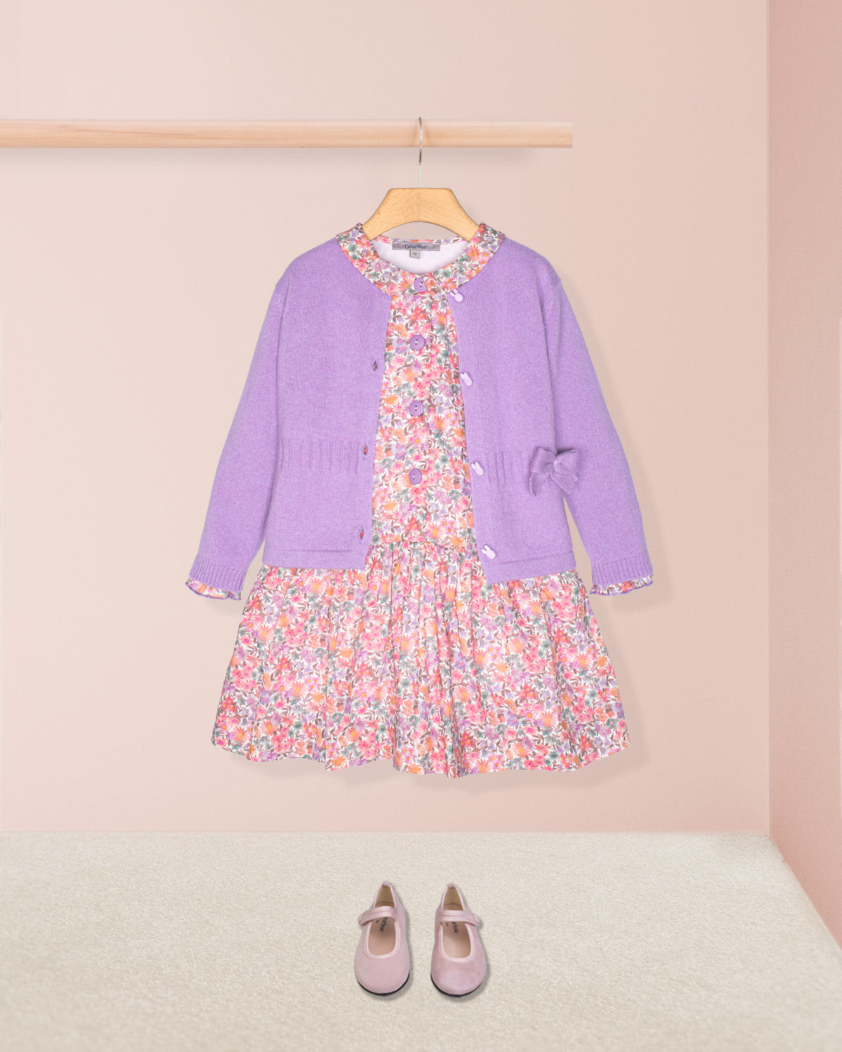 Purple cardigan and floral dress set with matching shoes on a pink background