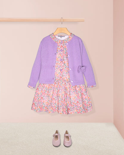 Purple cardigan and floral dress set with matching shoes on a pink background