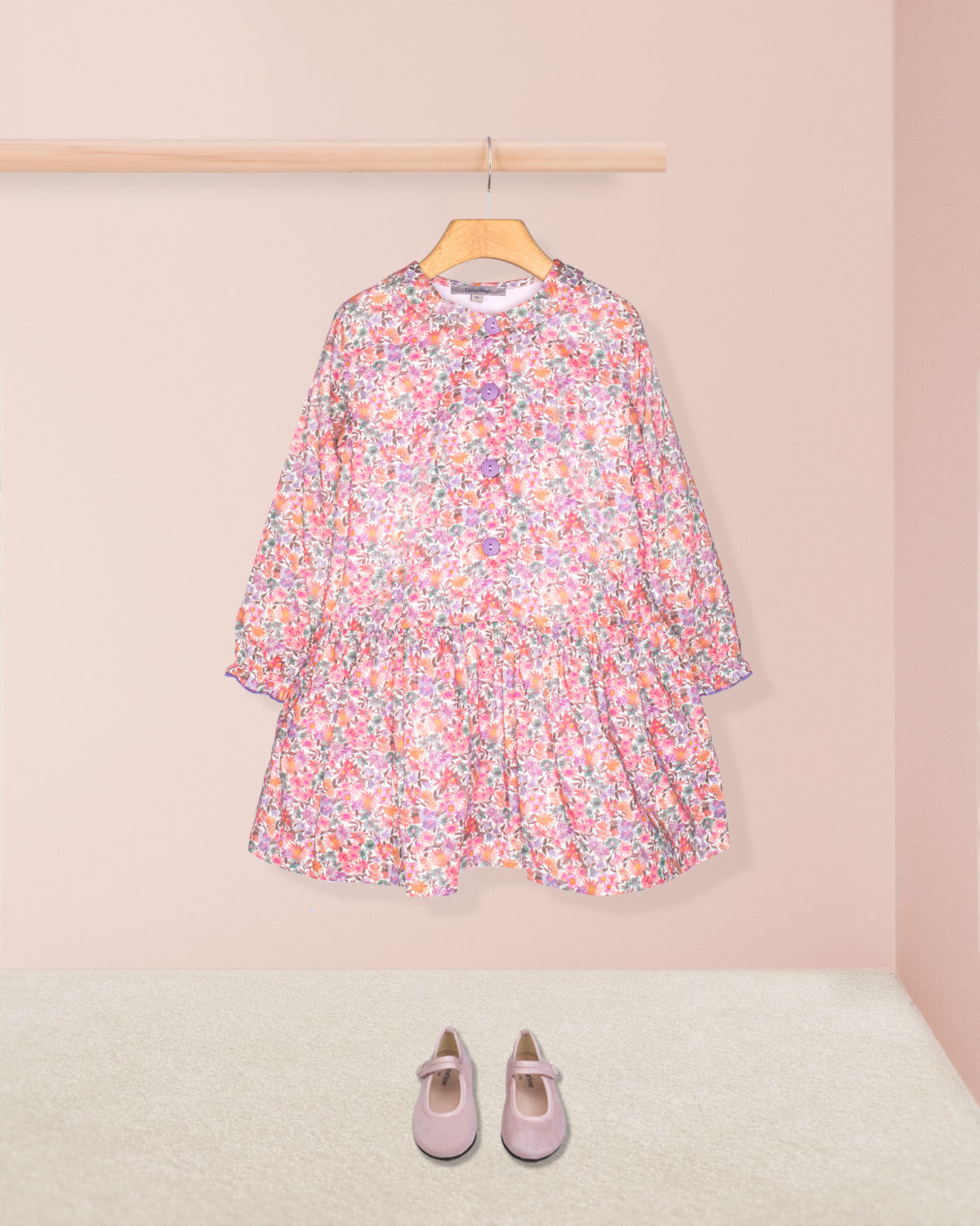 Floral dress on a hanger with pink shoes on the floor against a light pink wall.
